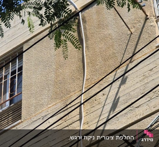 צינור מיזוג אוויר תלוי על קיר בניין עם צללים של עלים